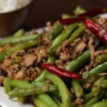 fresh green beans and crumbled cooked pork sausage with hot peppers in pan