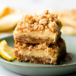 two lemon crumblebar cookies on a green plate with slice of lemon on the side